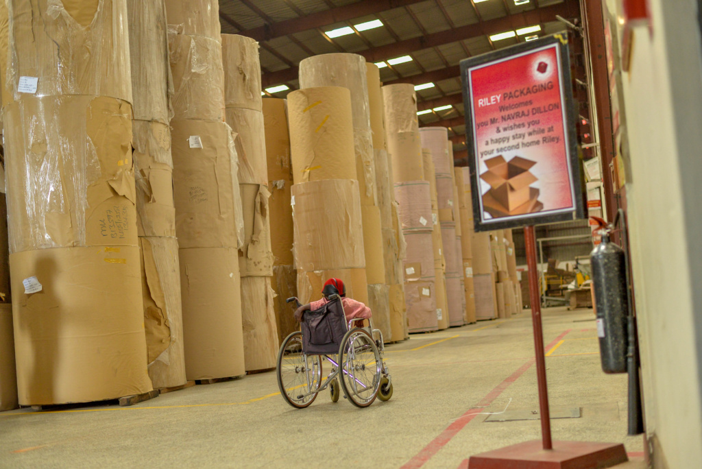 Sula working at Riley Packaging, riding a wheelchair though the warehouse.