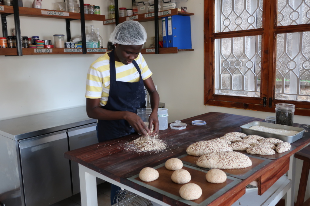 Person in a striped shirt and apron preparing dough on a wooden table in a kitchen setting.