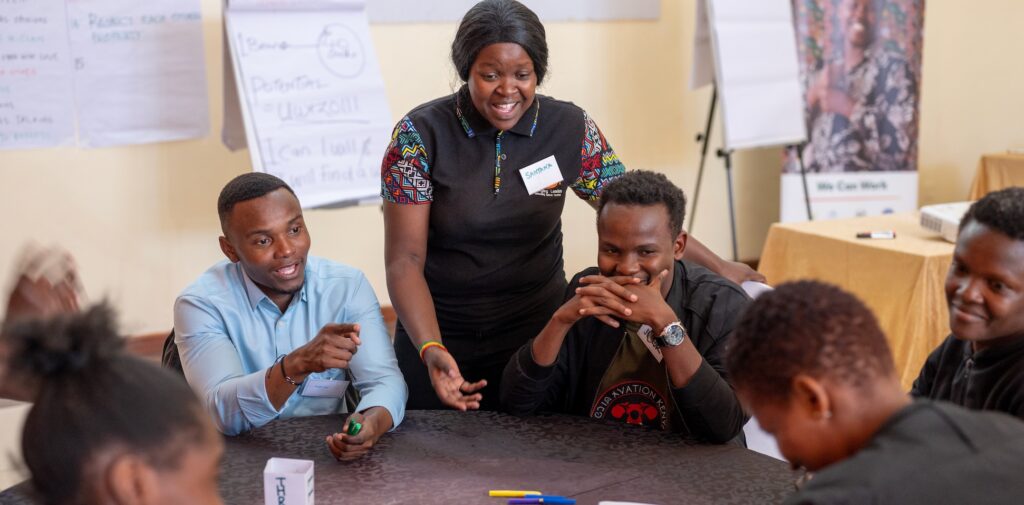 A woman standing at a table of laughing young people with disabilities doing an activity