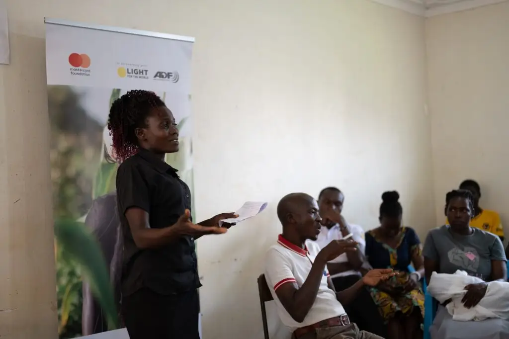 A young woman in black talks in front of a room full of youth with disabilities
