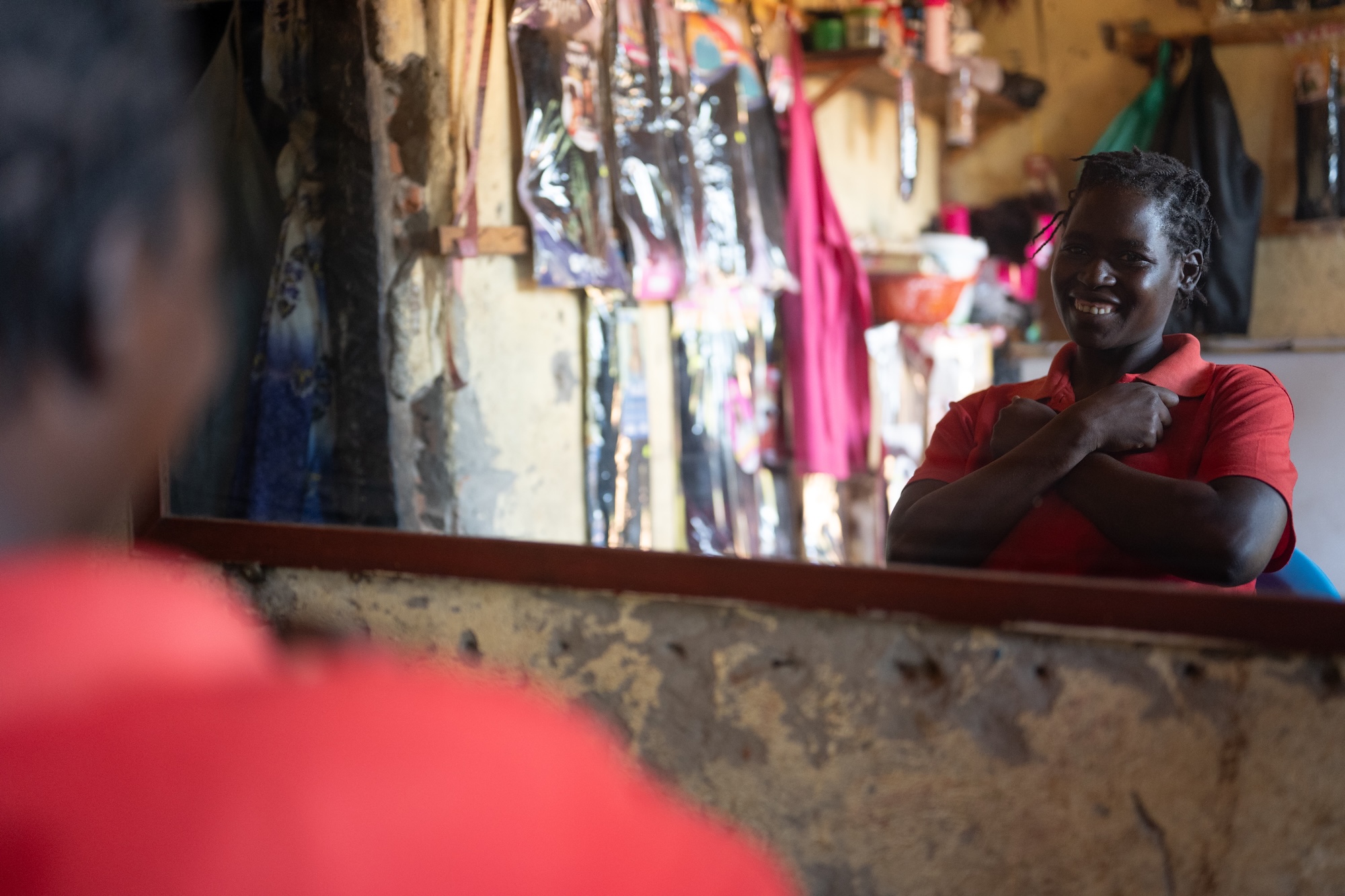A young woman in a red shirt looks on the mirror and signs the Ugandan Sign Language sign for love
