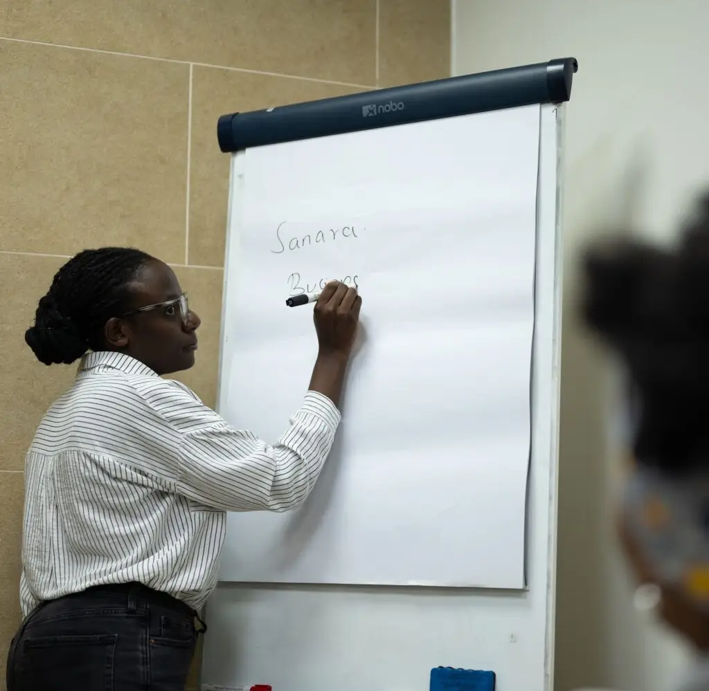 A young woman with glasses writes on a flip chart paper