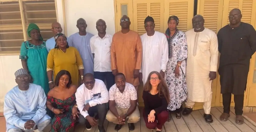 A group of mostly men and some women standing and and posing for a group photo. Most are wearing Senegalese styled clothing.