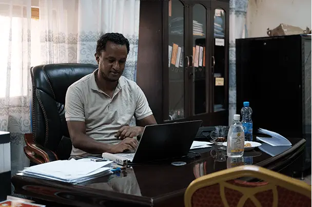 Dr. Mikya sitting behind a desk with a laptop.